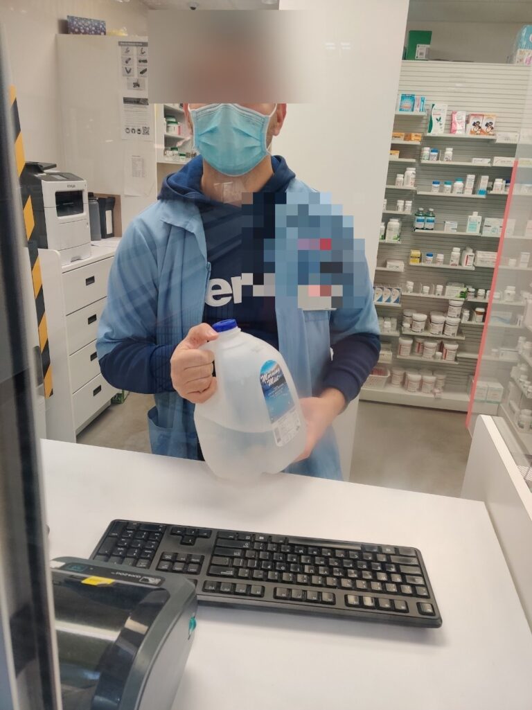 Costco Pharmacy pharmacist holding a Morning Mist 1-gallon distilled water jug at the prescription counter in Mississauga