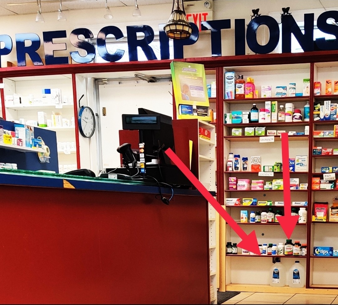 Pharmacy prescriptions counter with Morning Mist distilled water gallons stocked on retail shelves next to over-the-counter health products