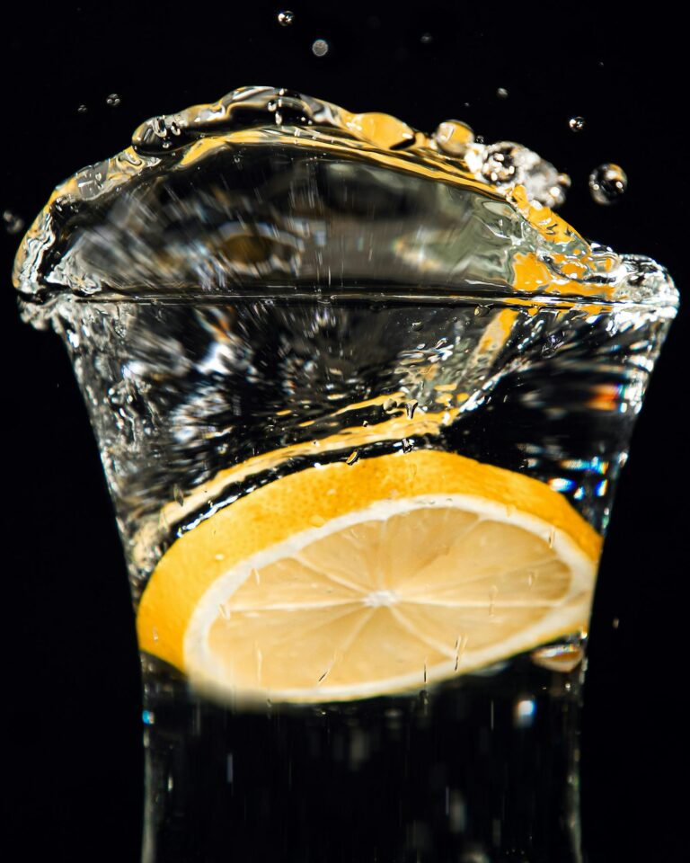 Lemon dropping into a clear glass of distilled water with a dramatic splash on a black background