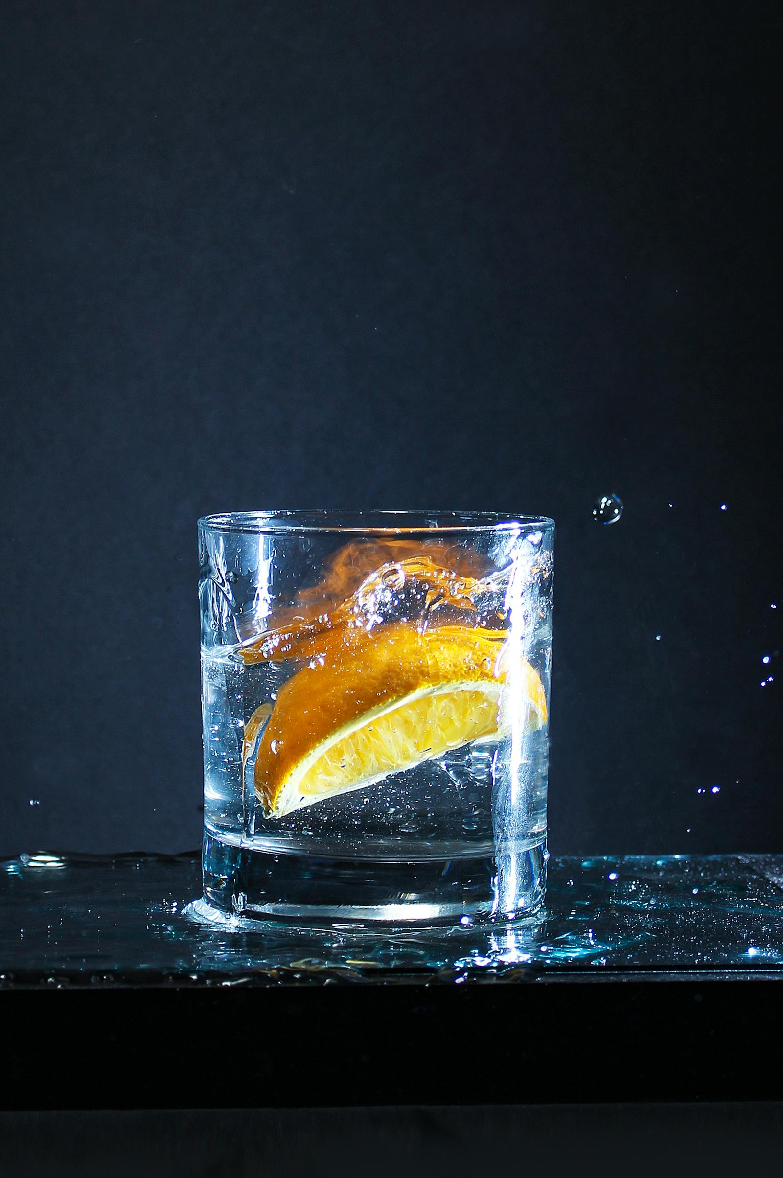 A fresh citrus wedge dropping into a clear glass of distilled water with droplets and splash on a dark background