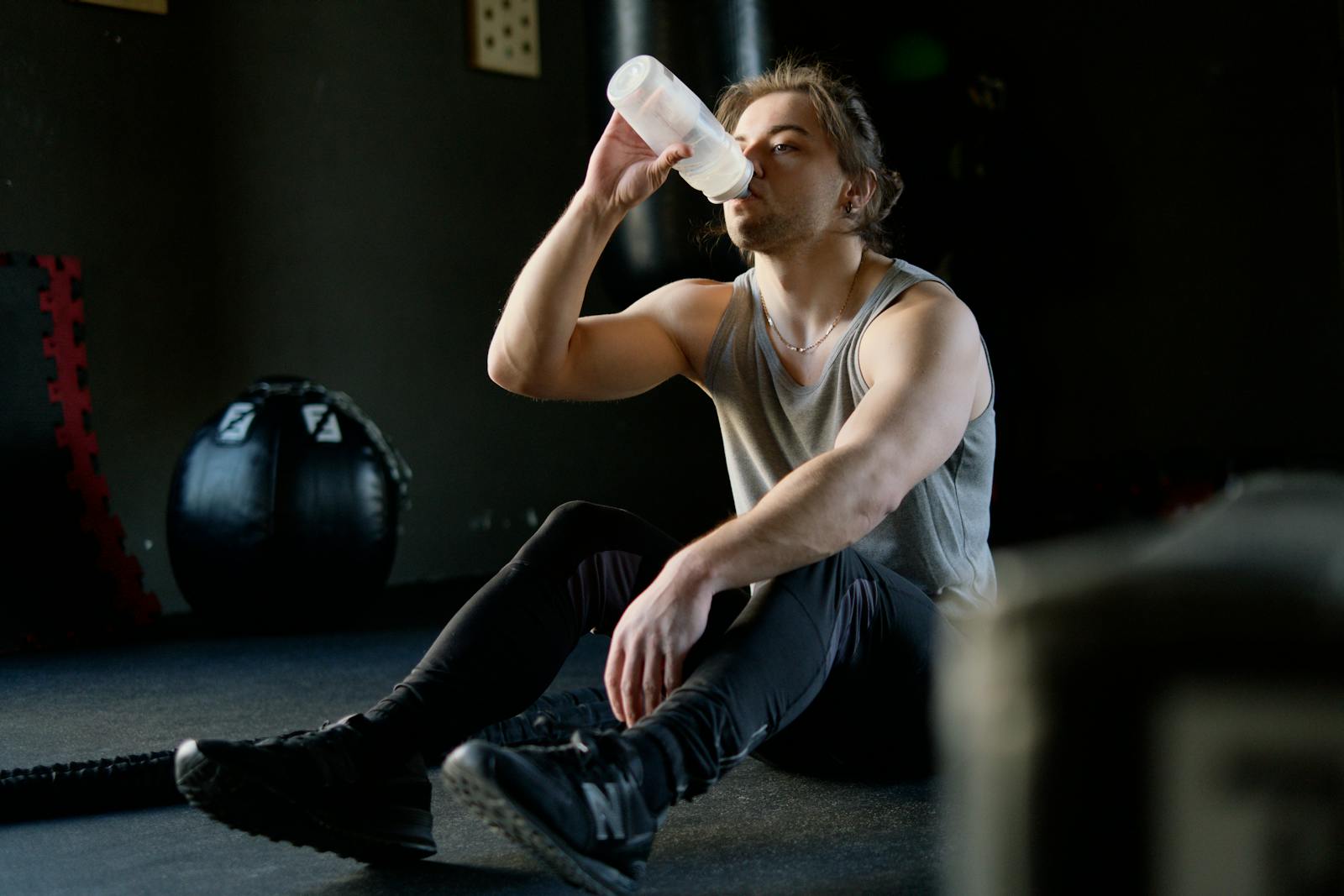 Athletic person sitting on a gym floor taking a hydration break with a water bottle after exercise