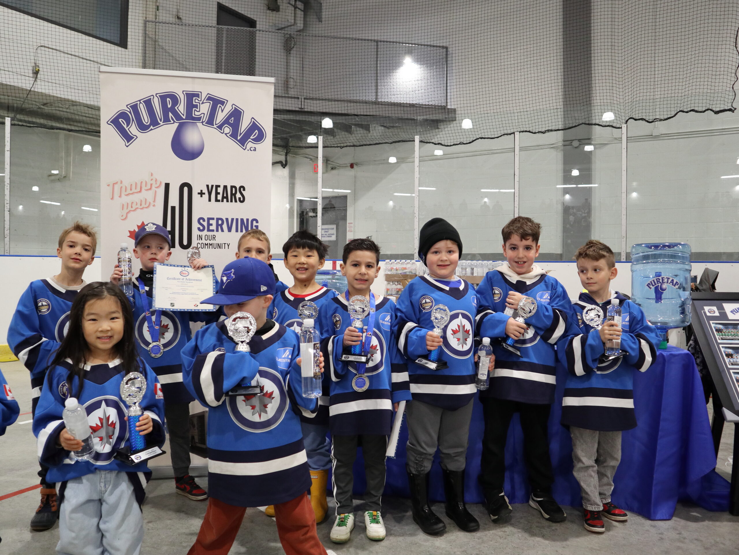 Mississauga youth hockey team in blue and white jerseys gathered behind their Puretap water bottles in front of the Puretap pull-up banner at Port Credit Memorial Arena.