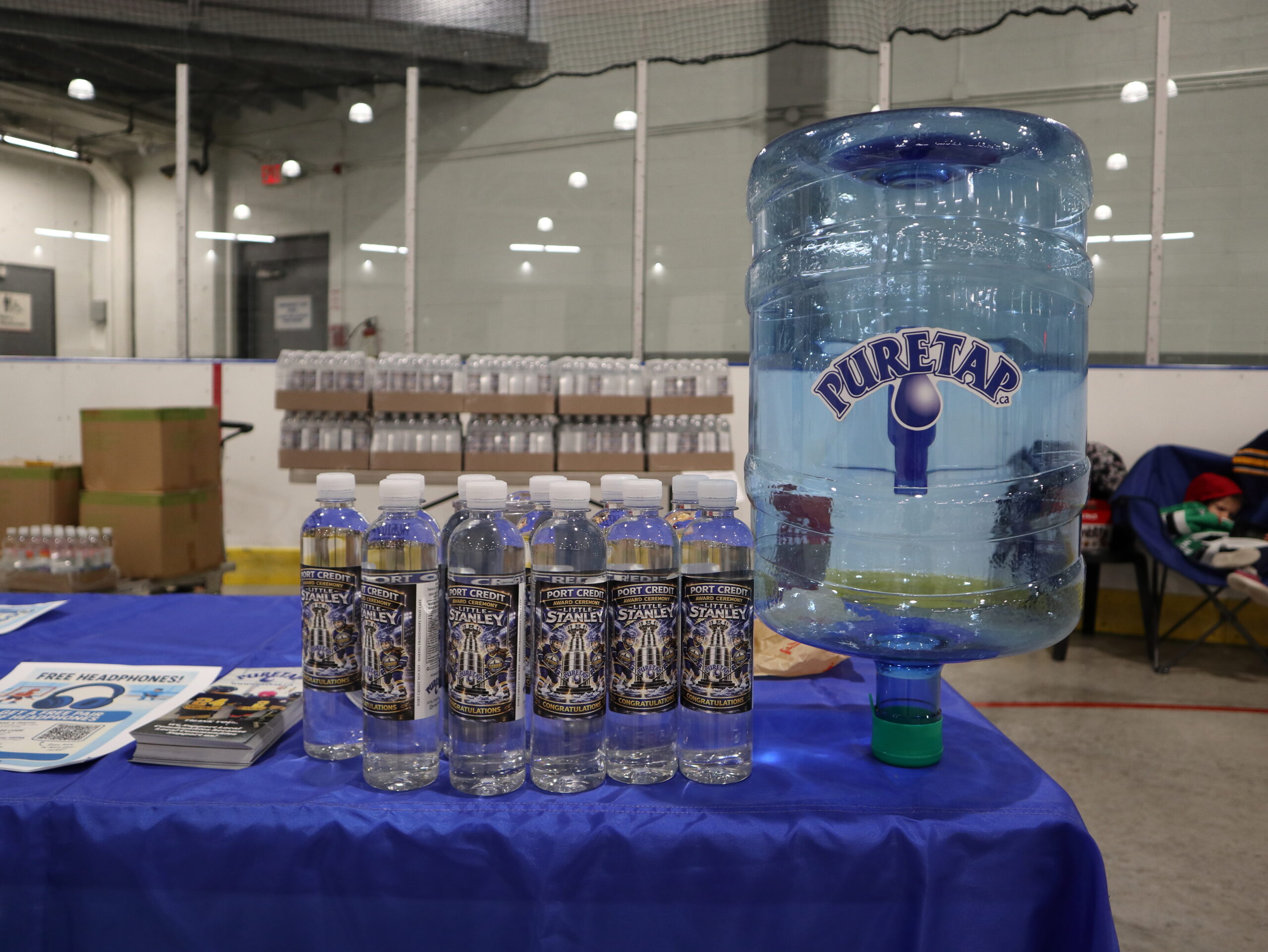 Close-up of the co-branded water bottles created for the 2026 Port Credit Hockey awards night — Puretap spring-distilled water inside, custom hockey-themed labels on the outside, lined up in front of a five-gallon Puretap jug.
